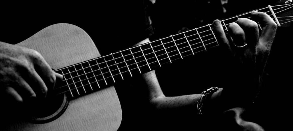 Black and white image of a person strumming an acoustic guitar, focusing on hands.